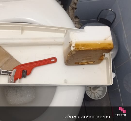 מפתח צינורות אדום על מכסה אסלה פתוח